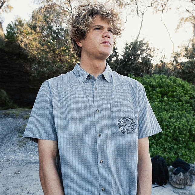 Man wearing a grey checkered shirt with a logo outdoors.