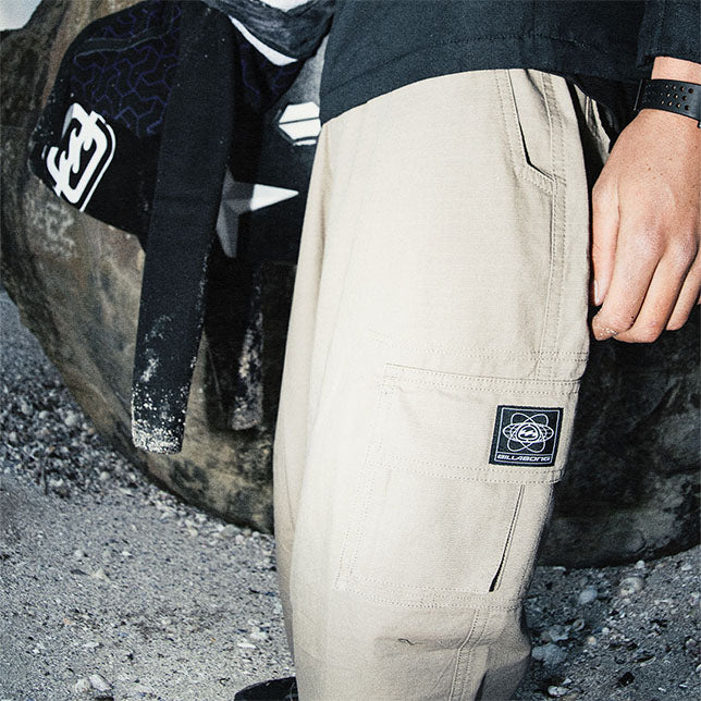 Man wearing khaki pants with a brand logo, standing near a large rock.